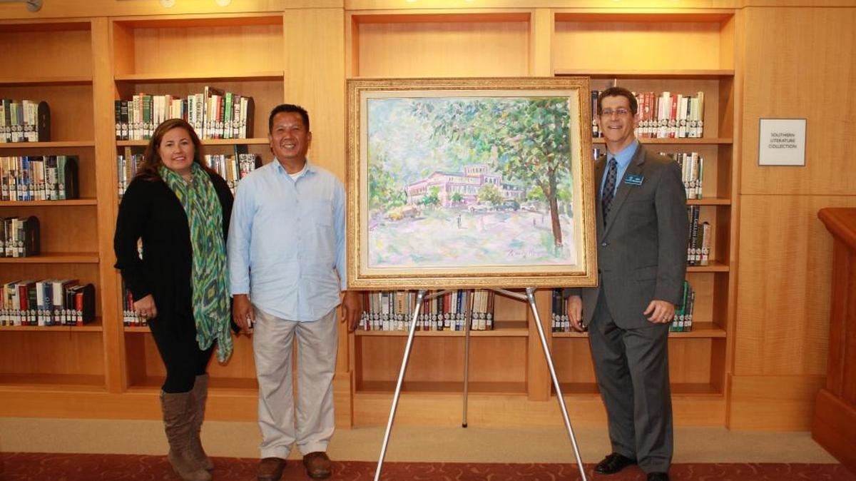 From left, Muscogee County Library Foundation chairwoman Katie Athey, local artist Randy Nguyen and Chattahoochee Valley Libraries director Alan Harkness pose with Nguyen’s painting of the Columbus Public Library. The foundation bought the painting and donated it to the library, where it will be displayed.