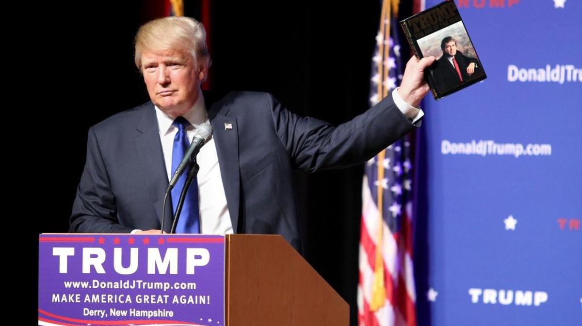 Republican presidential candidate Donald Trump holds up a copy of his 1987 book, “Trump: The Art of the Deal” during a town hall event.