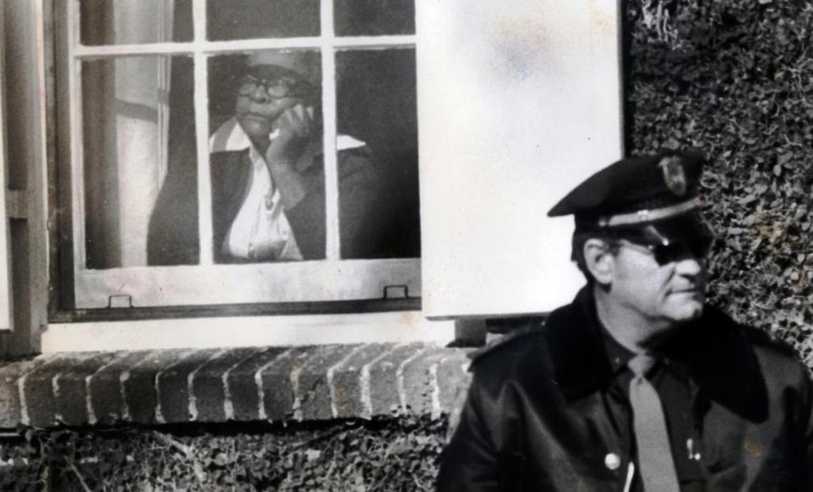 A woman weeps at the window of Kathleen Woodruff’s home as a police officer stands guard outside on Dec. 28, 1977.