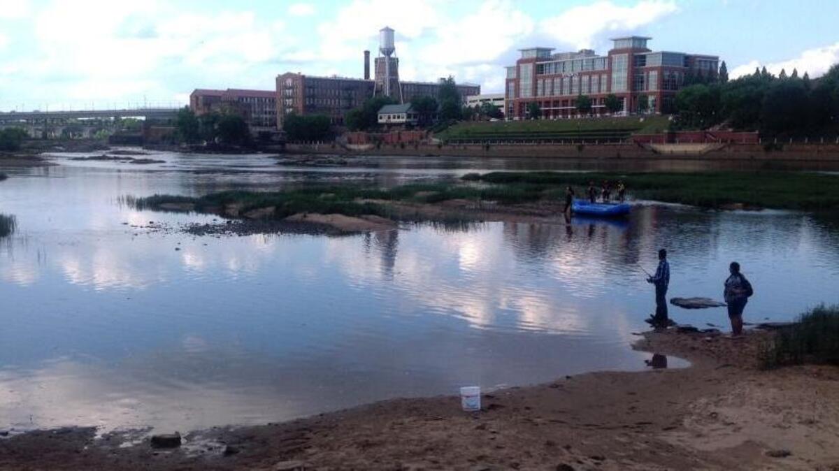 A couple fishes out on the river as a fire-rescue team in the background looks for a body.