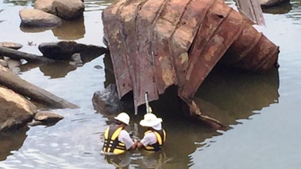 Georgia Power Co. crewmen wade out to attach a cable to large metal object in the river.